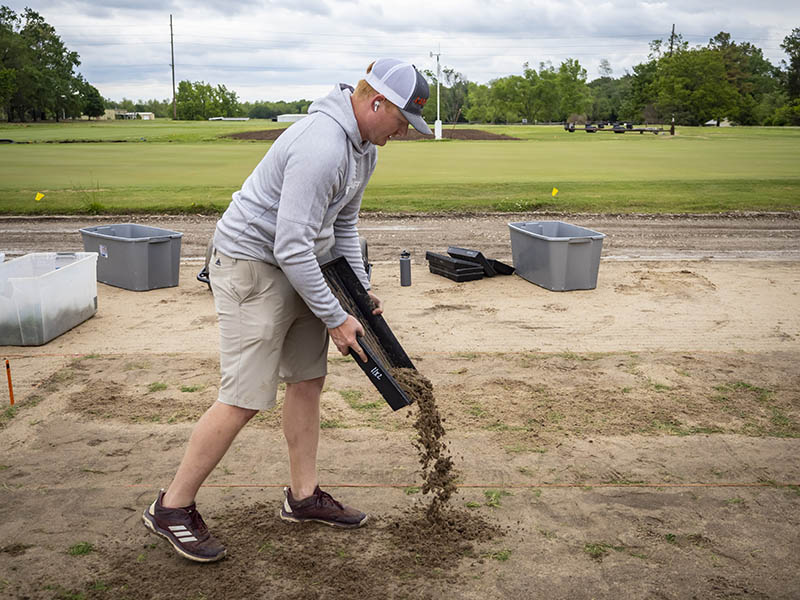 Image of graduate student pouring soil at the turfgrass fields.