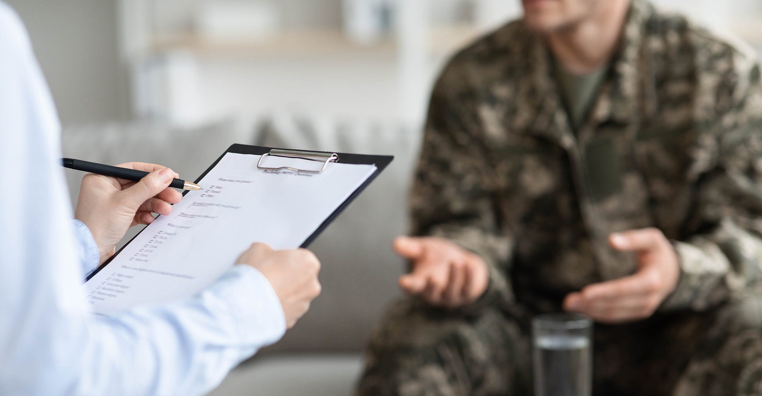 Body of someone in a military uniform sitting in a doctor's office with a doctor holding a notepad.