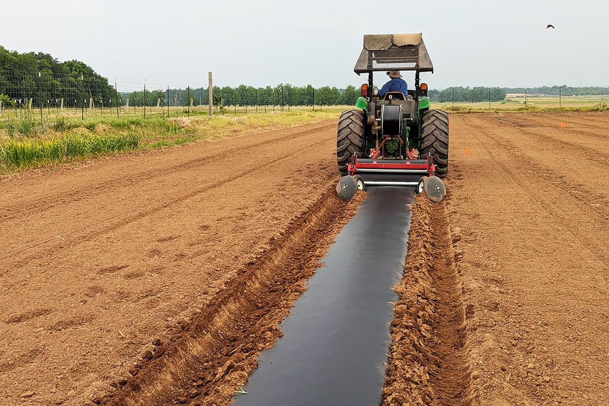 the back of a tractor as it tills across a field to prepare it for planting