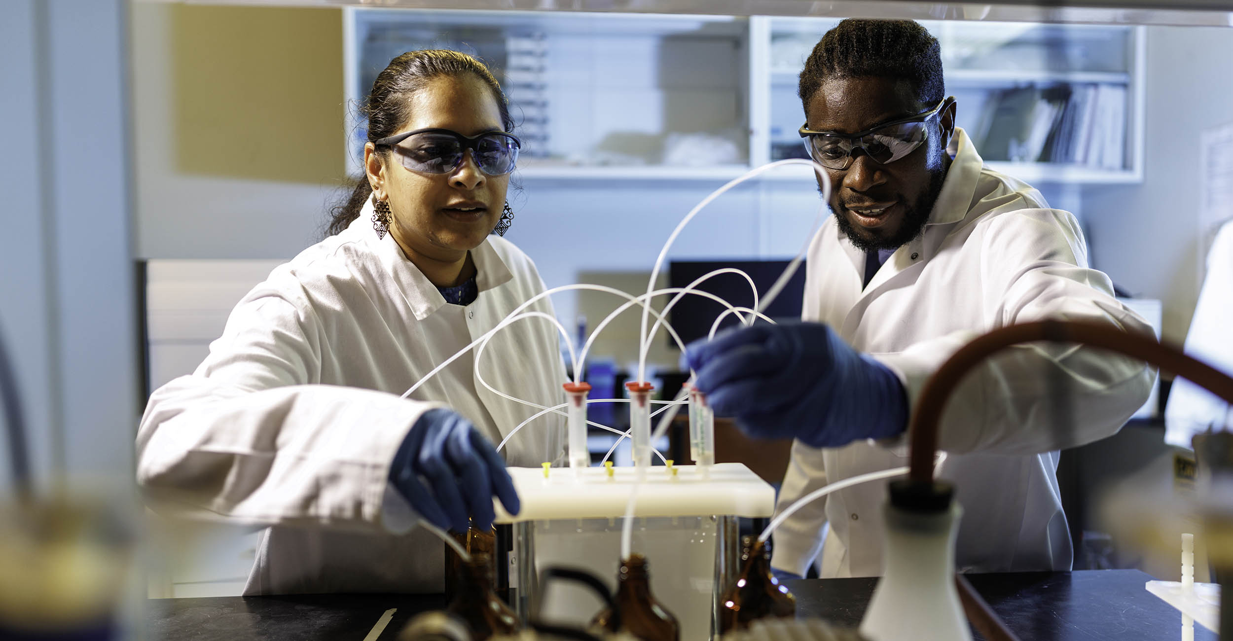 Mangalgiri cleans waste water with her student using equipment in her lab.