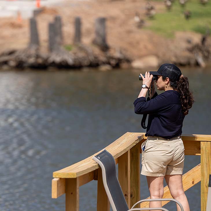 Narges Taravatrooy using binoculars to look at the yellow floating heart on Lake McMurtry 