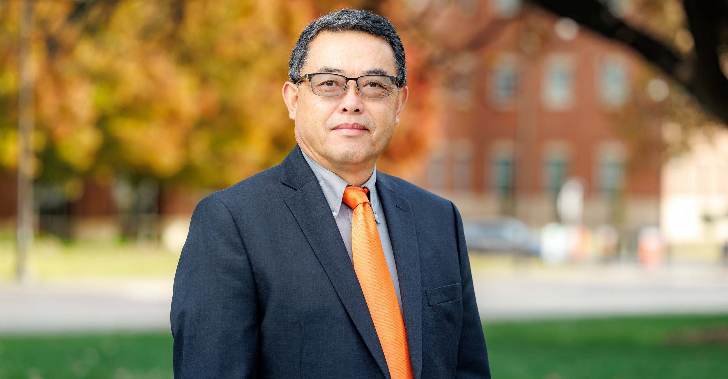 Yanqi Wu poses for a picture. He is outside, standing in front of a tree, wearing a dark suit.