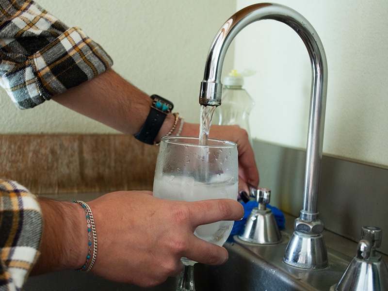 Hands holding a drinking glass under a water faucet.