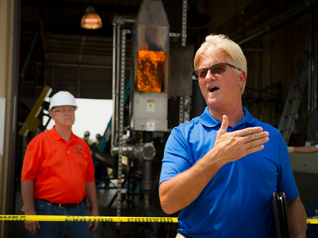 A man in a blue shirt giving a lecture in front of a machine.