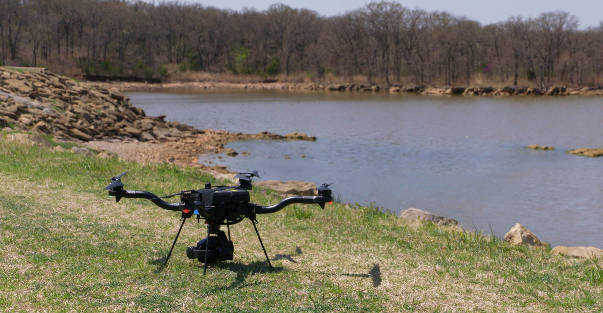 A drone sitting on the ground in front of water.