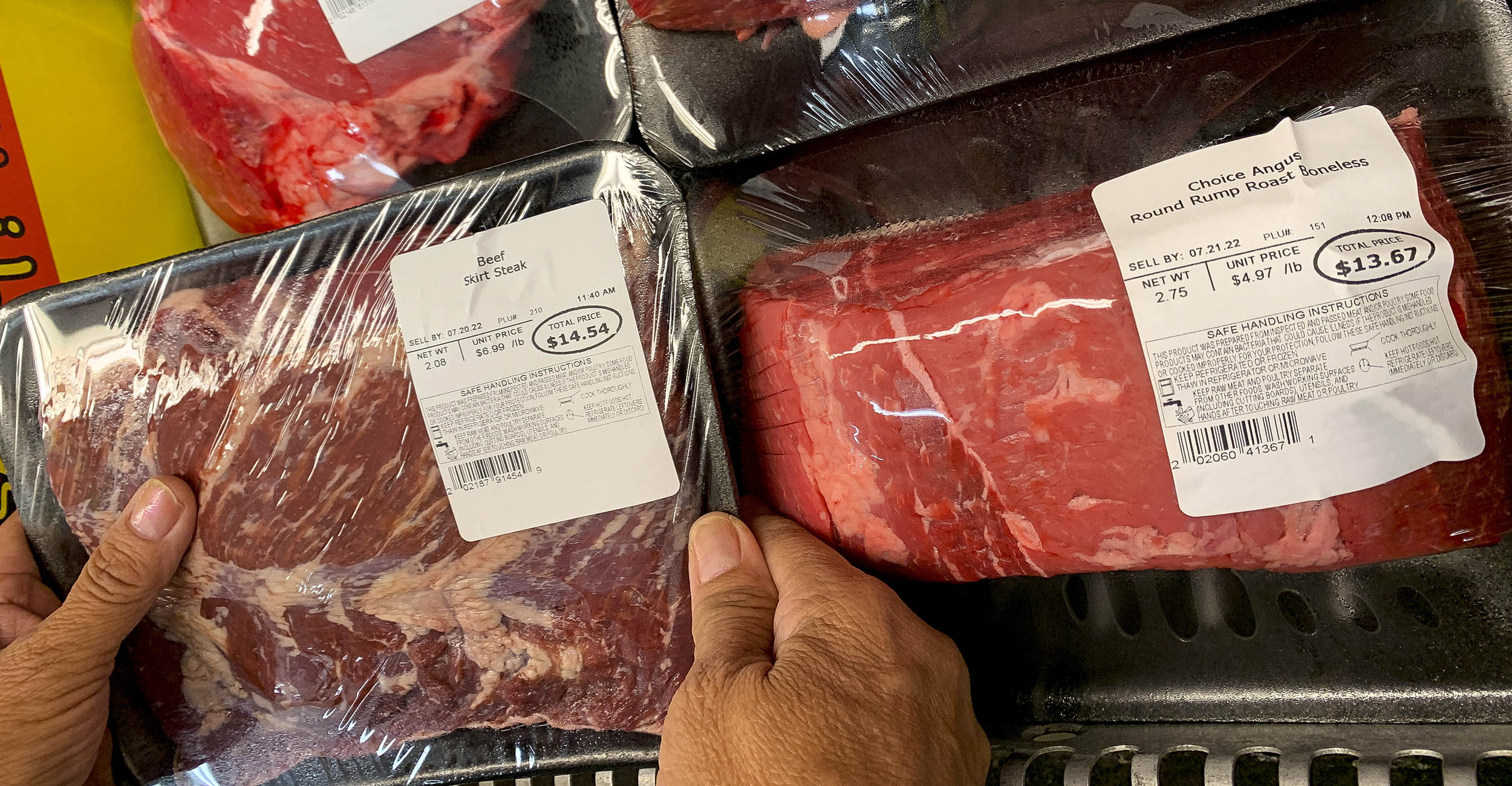 A pair of hands hold packages of beef in the grocery store.