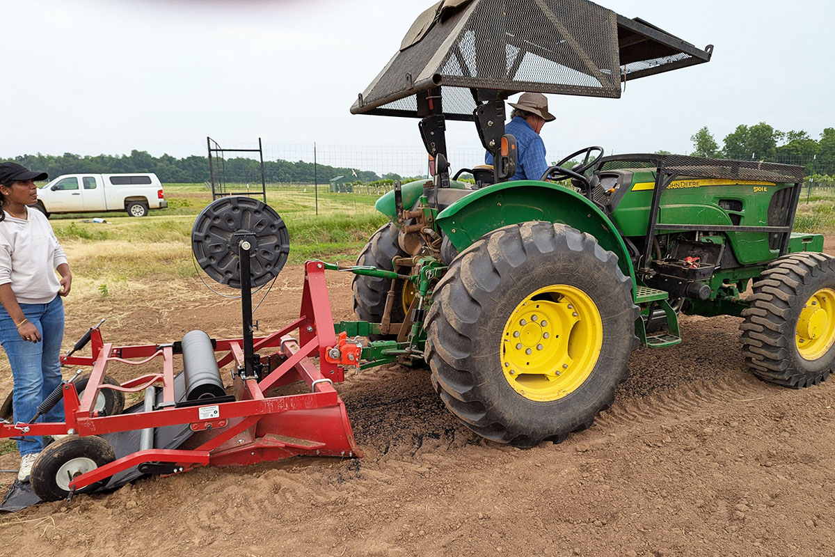 Person sitting on a tractor with a tiller attached to it pre-planting