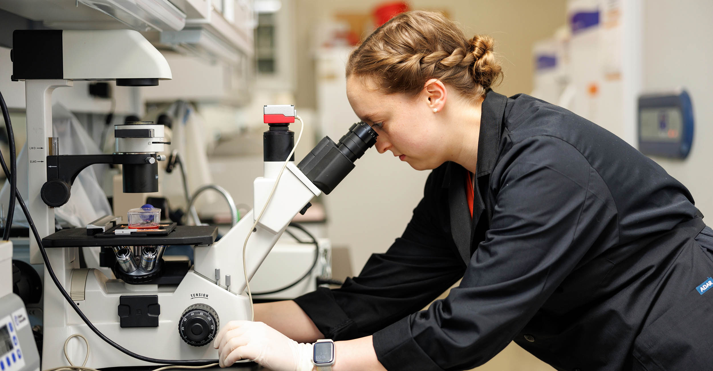 9-11-tesa-banner.jpg MaKenna McKendrick looking into a microscope in a lab.